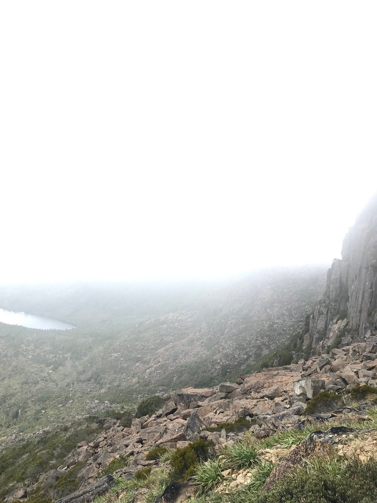 Columns of dolerite forming a cliff on the right, with a forested valley and a small lake far below, half obscured by low cloud
