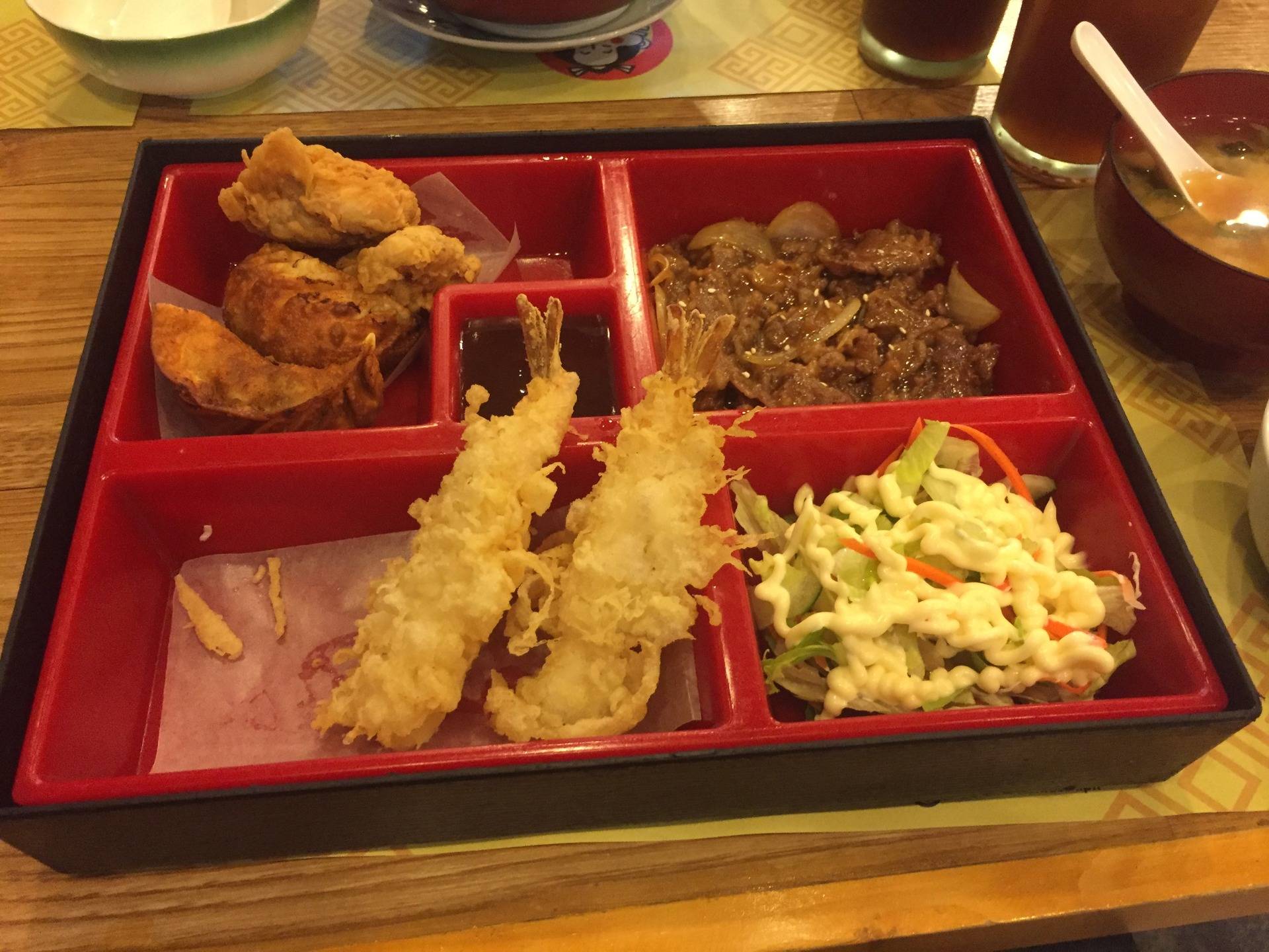 Bento box consisting of two shrimp tempuras, fried chickens, beef steak and mixed veggies with salad dressing.