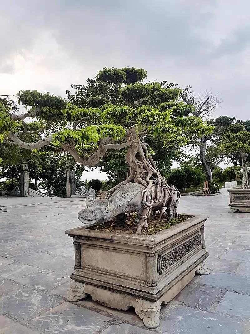 Bonsai garden features many neat trees accompanied by statues exhibiting emotions.