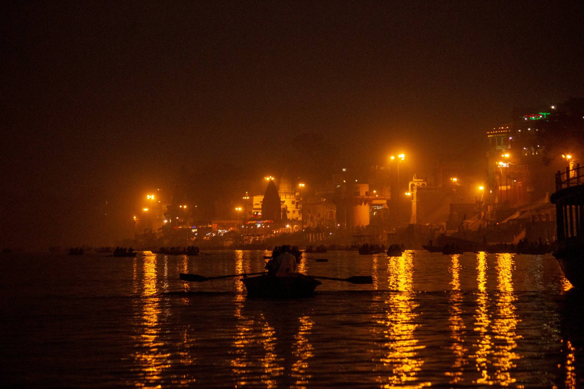 Tourist boats row towards the burning Ghats in the light of flames.