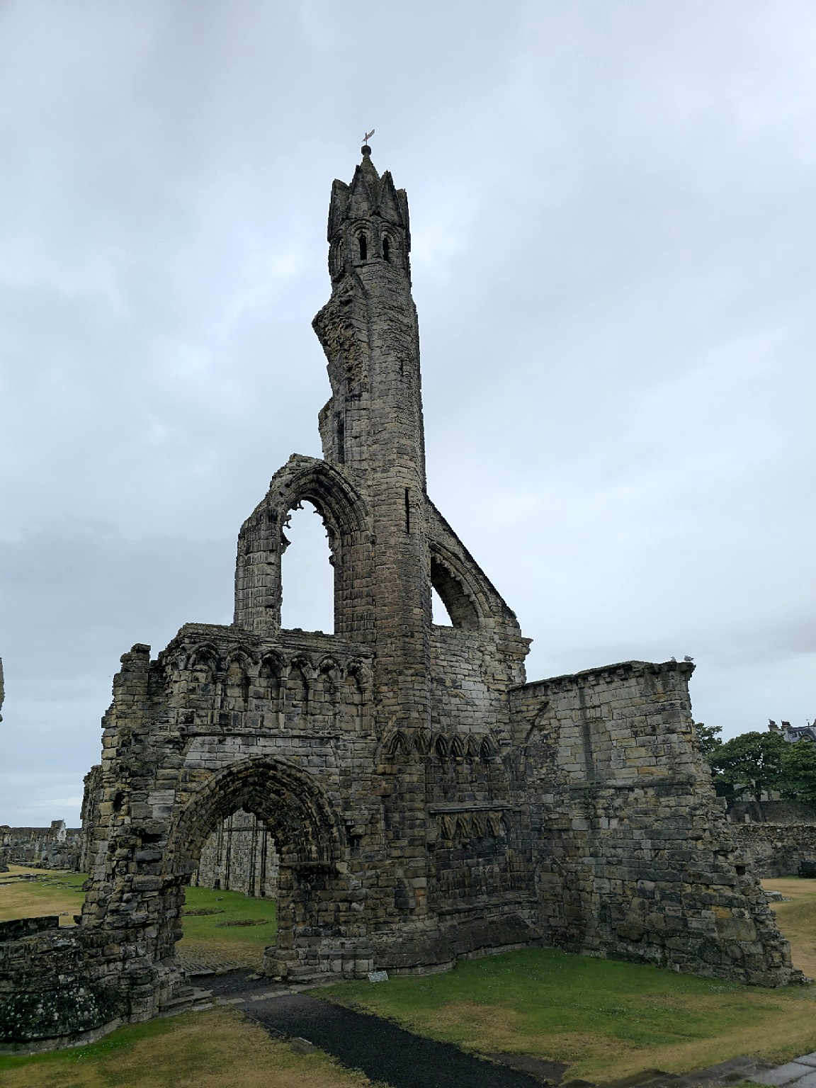 One surviving arch and tower against the Scottish sky — enough architecture to suggest the scale of what was lost.