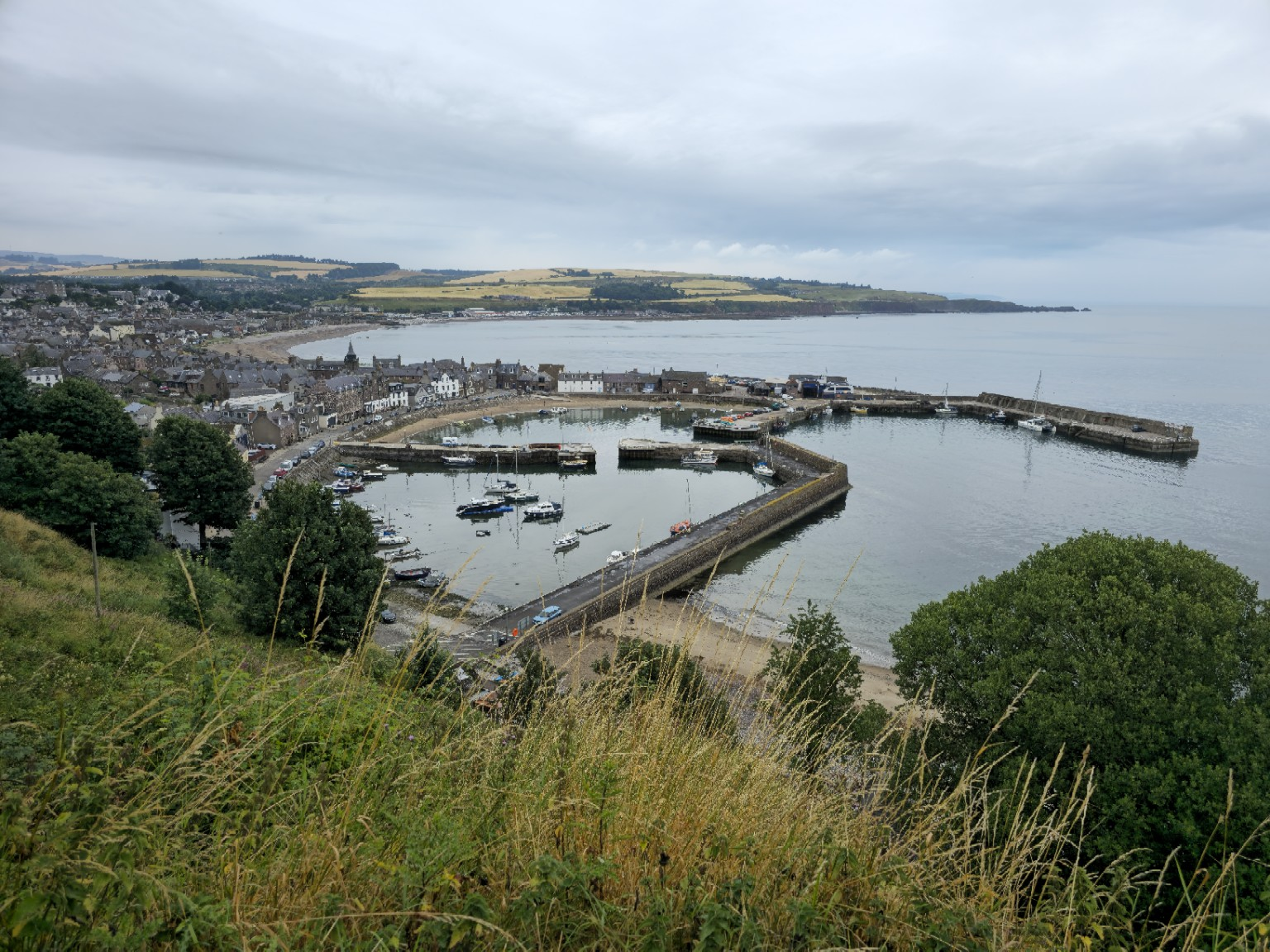 Stonehaven arriving all at once: harbour walls, stone houses and the broad curve of the bay.
