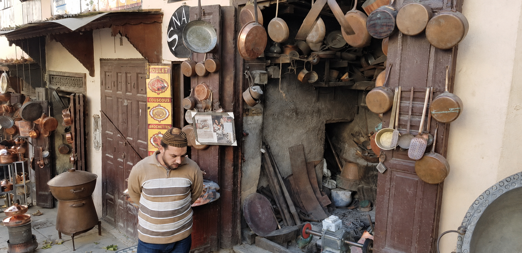 A metalworker’s shop in Fes el-Bali — copper pans, tools and workshop clutter spilling directly into the street, with production and sales still sharing the same few square metres.