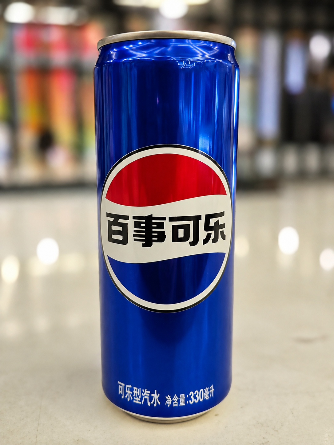 Blue can of Chinese cola with Chinese characters on its label, standing on a counter.