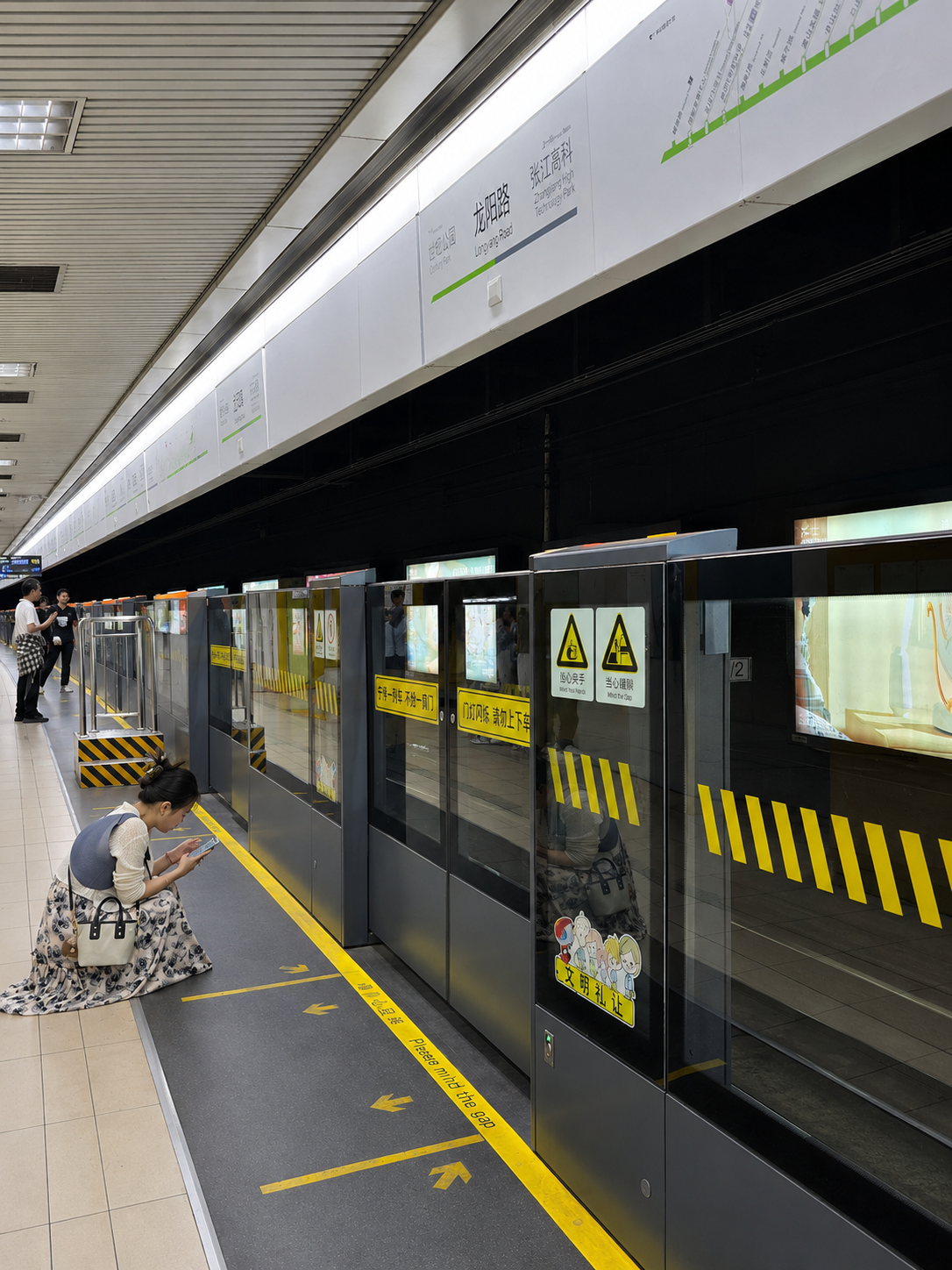 Shanghai metro platform screen doors with yellow safety markings and a woman crouching beside them.