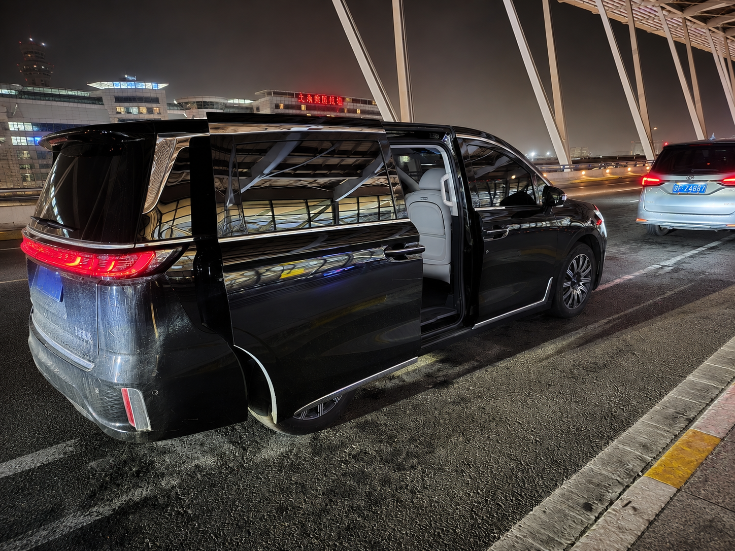 Black minivan with its sliding door open at a lit airport pickup area at night.