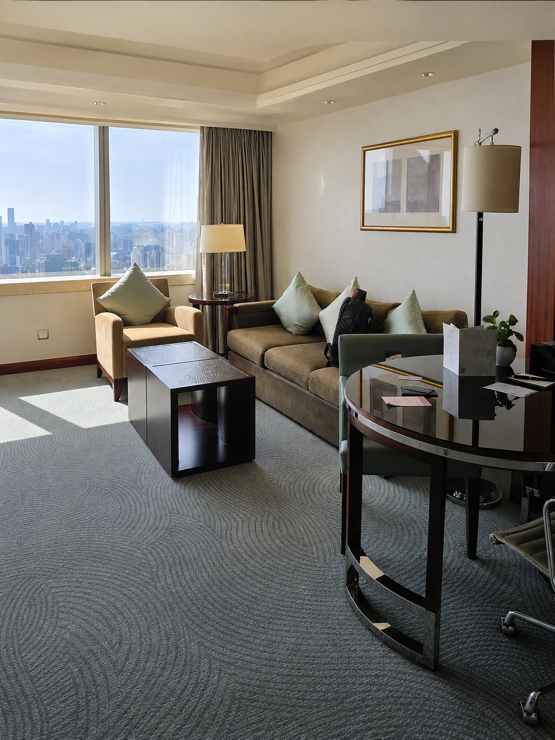 Hotel suite living room with sofas, armchairs, coffee table, desk, and a Shanghai skyline through the window.