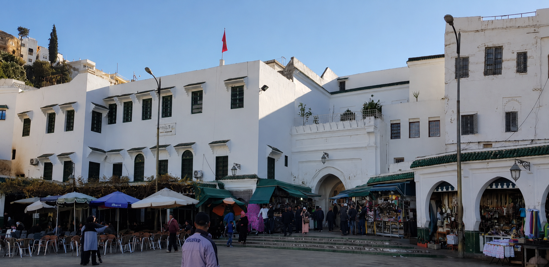 Whitewashed buildings and café umbrellas line the main square in Moulay Idriss, with people gathered outside shops.