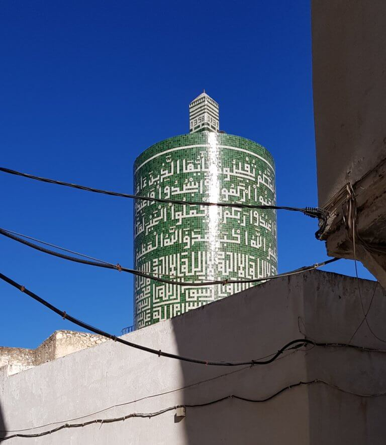 Green-and-white zellij-covered cylindrical minaret of Sentissi Mosque rises above rooftops in Moulay Idriss.