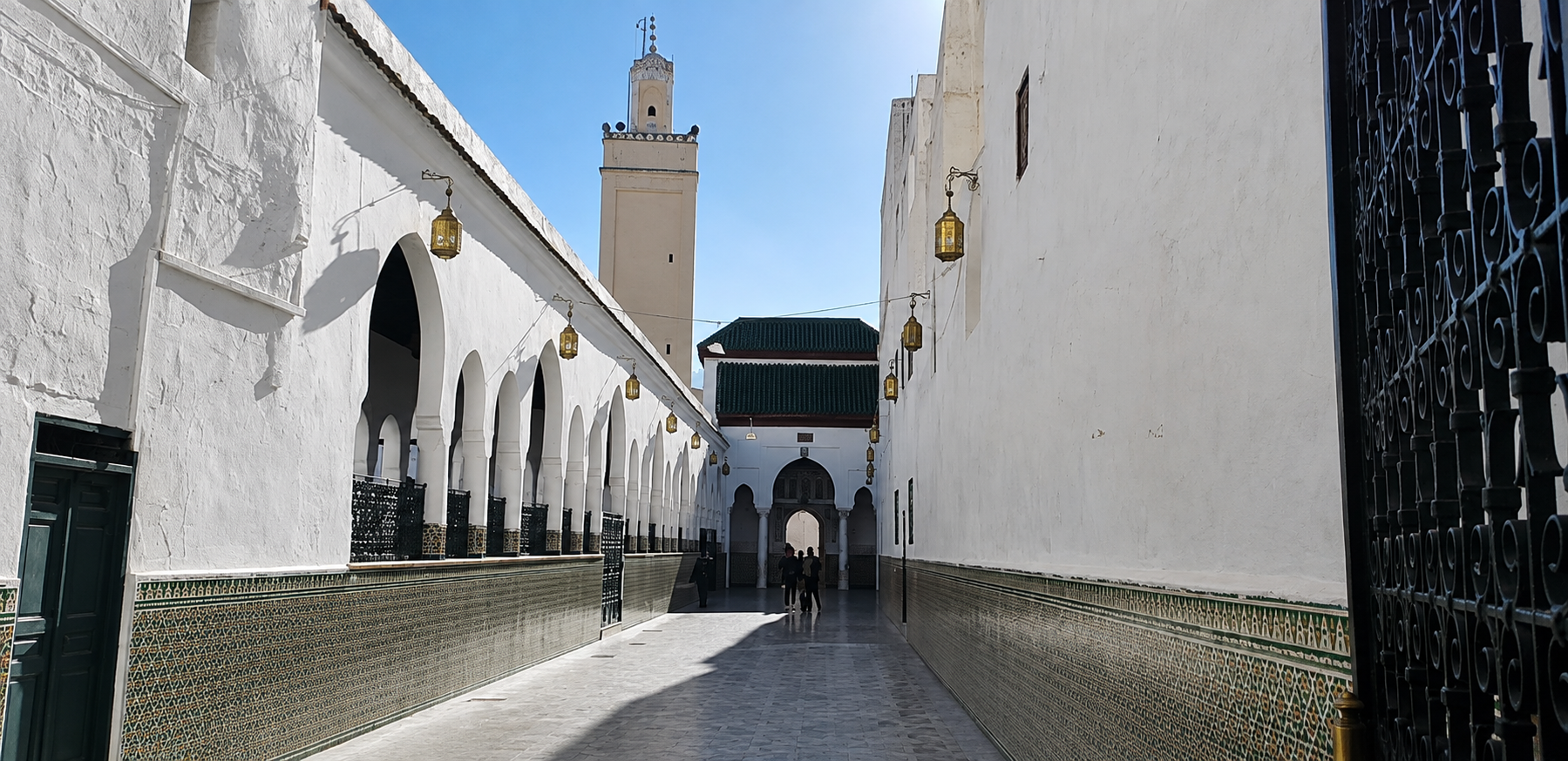 White-walled entrance courtyard to the sanctuary of Idris I in Moulay Idriss, with arched colonnades and a minaret.
