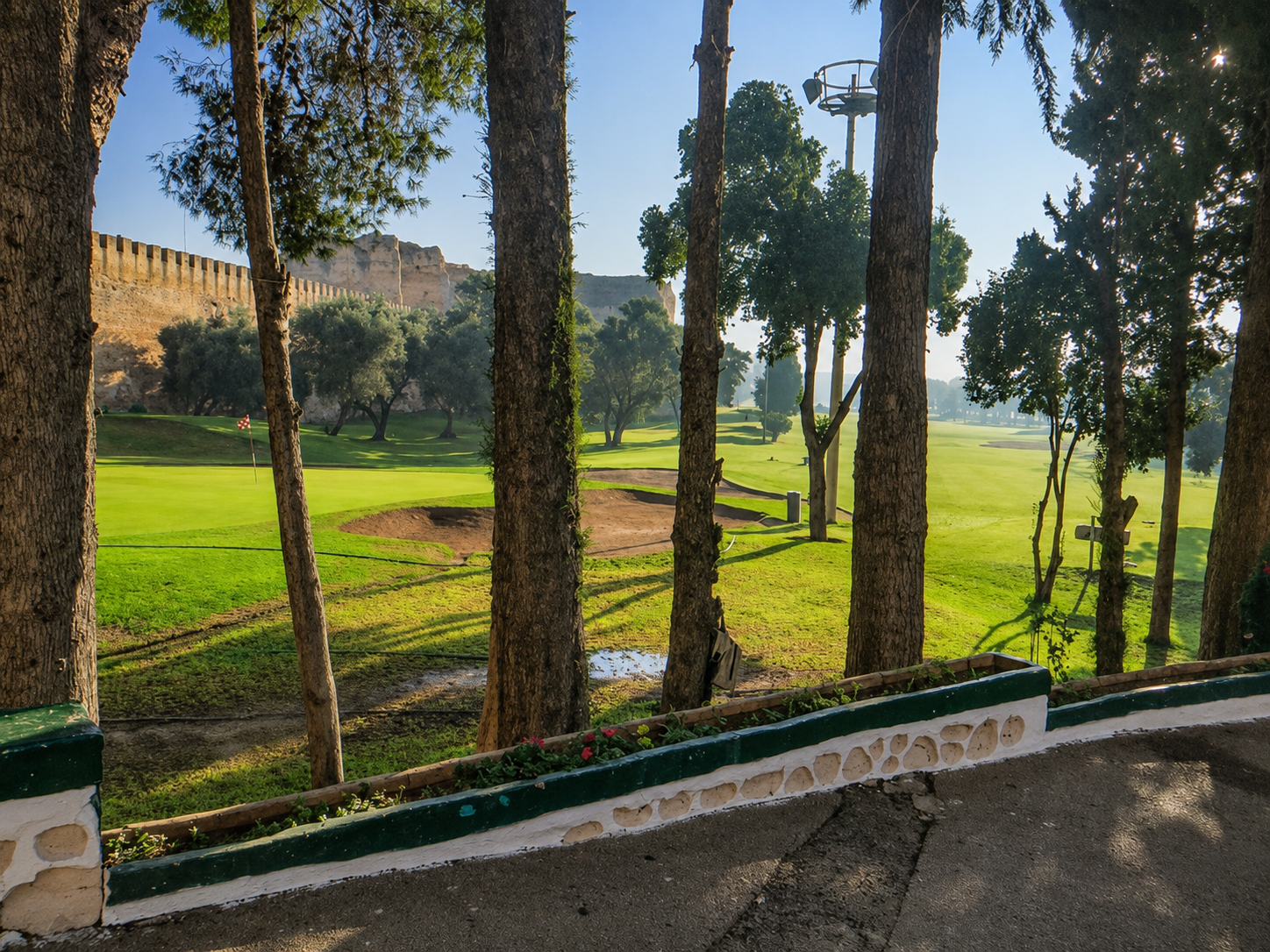 Green golf course framed by trees and bordered by old stone walls at Royal Golf de Meknès.
