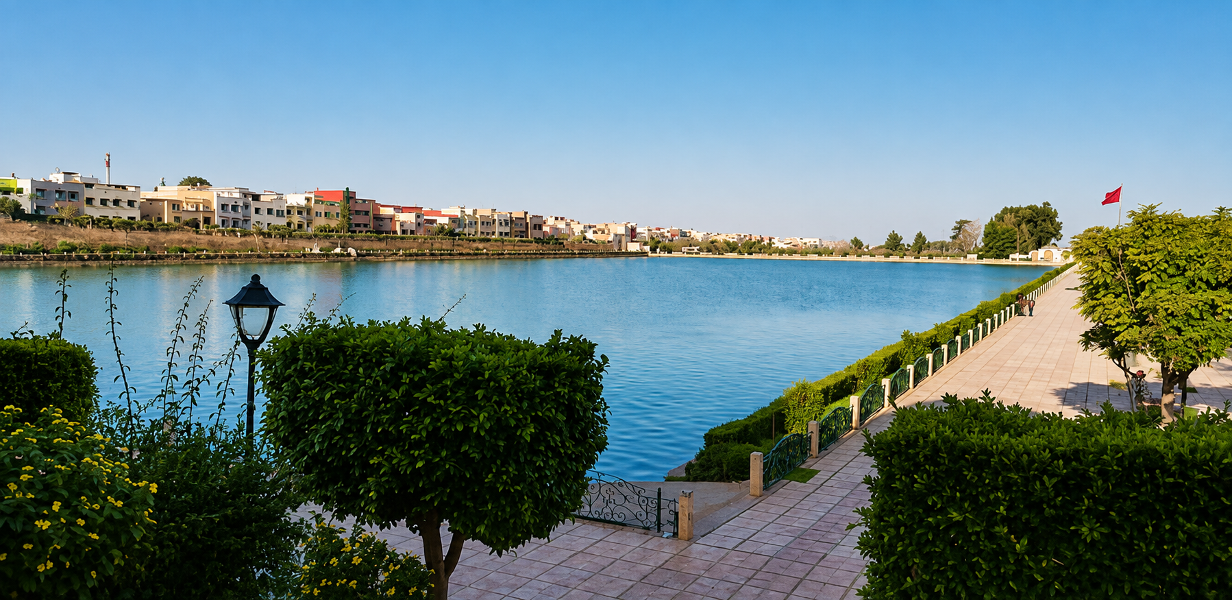Sahrij Souani reservoir in Meknes, with a paved promenade, trimmed shrubs, and buildings across the water.