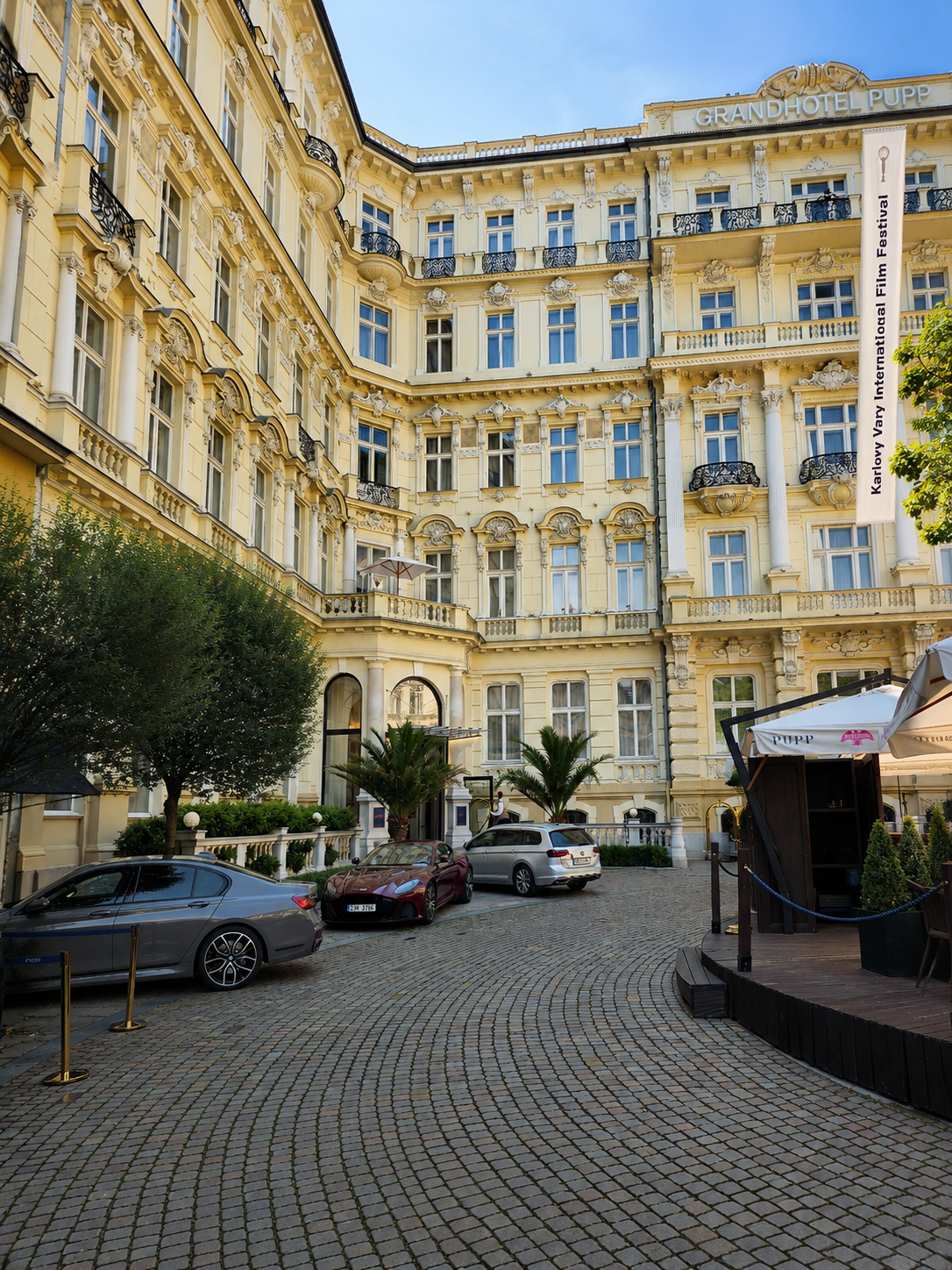 Grandhotel Pupp’s ornate cream facade and cobbled forecourt with parked cars in Karlovy Vary.