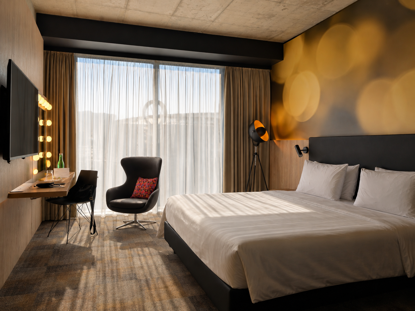 Modern hotel room with a king bed, desk, armchair, and floor-to-ceiling window.