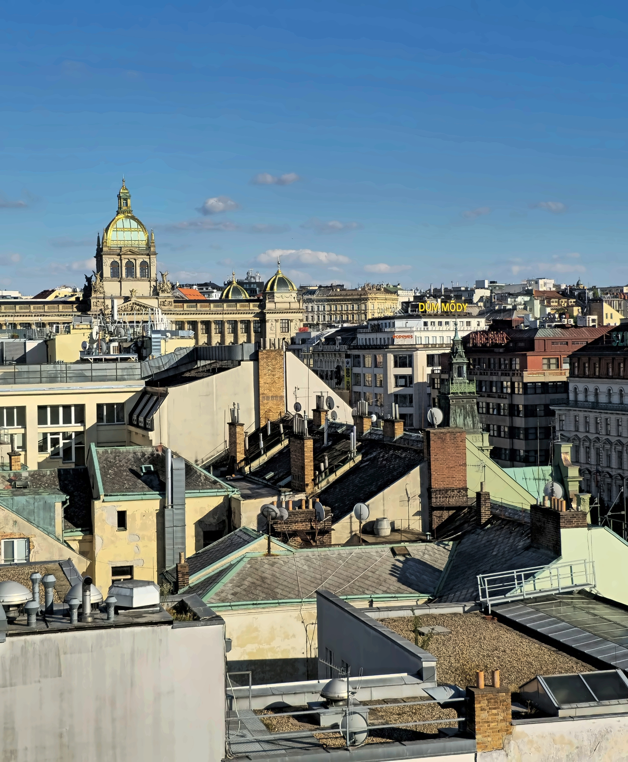 Prague seen from the rooftop of W Prague — a layered jumble of domes, chimneys, weathered roofs and hidden infrastructure stretching across the New Town.