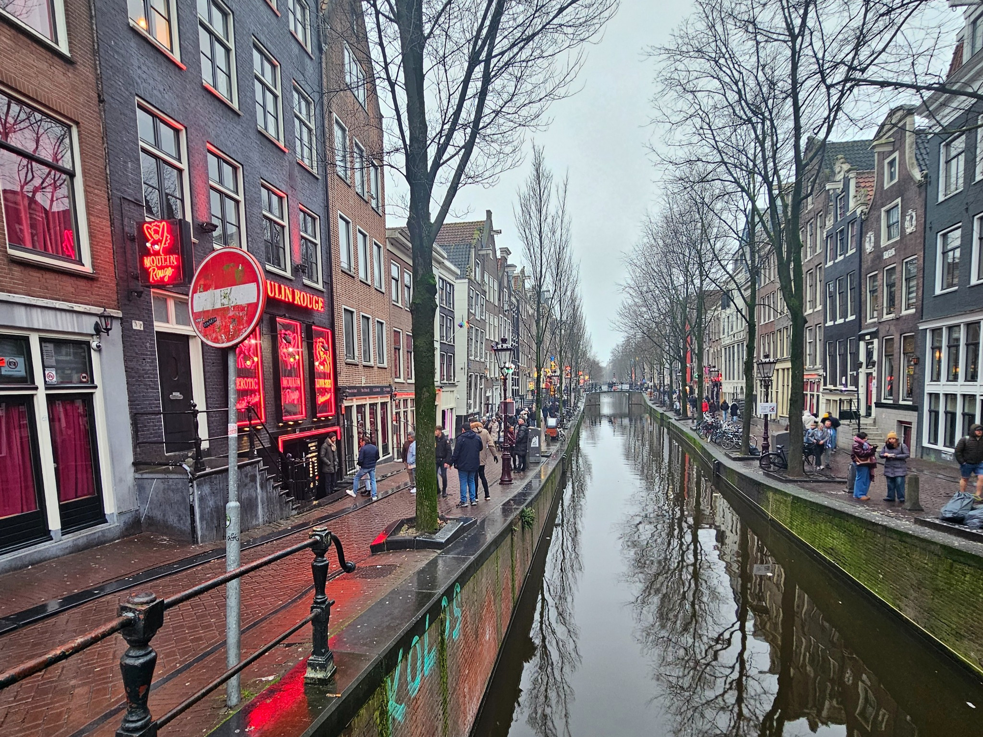 A canal lined with narrow brick buildings and red-lit storefronts in Amsterdam’s De Wallen district.