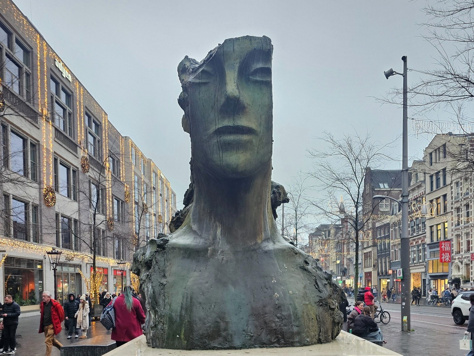A damaged giant head-and-shoulders sculpture stands on a busy Amsterdam street.