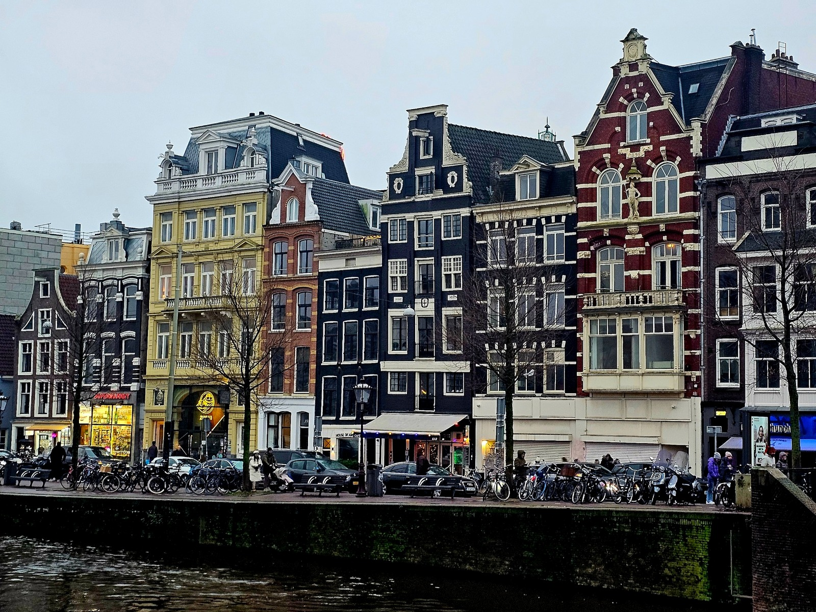 Narrow ornate canal houses and parked bicycles line Oude Turfmarkt in Amsterdam beside a canal.