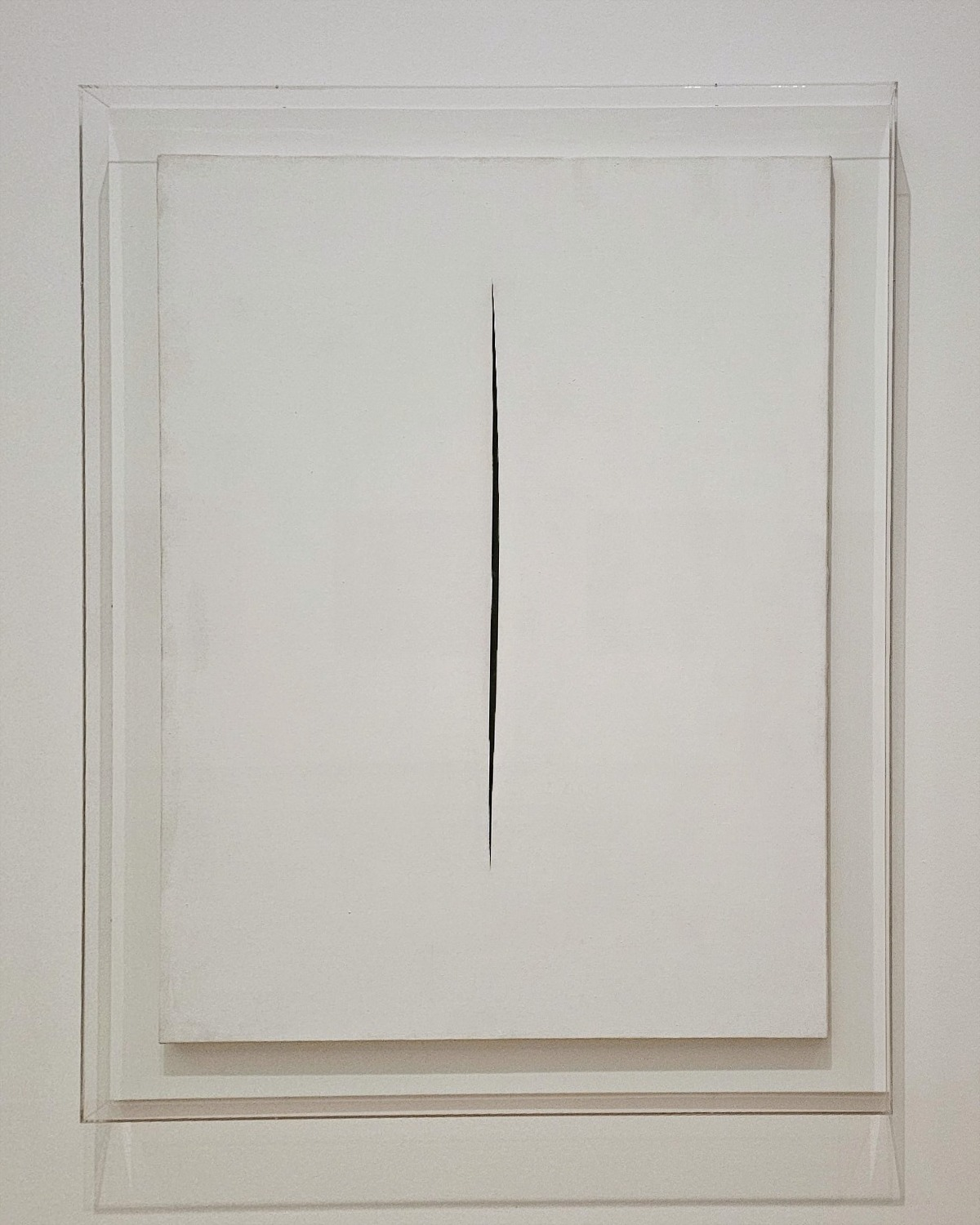 White abstract artwork with a narrow vertical cut, mounted in a layered frame on a white wall.