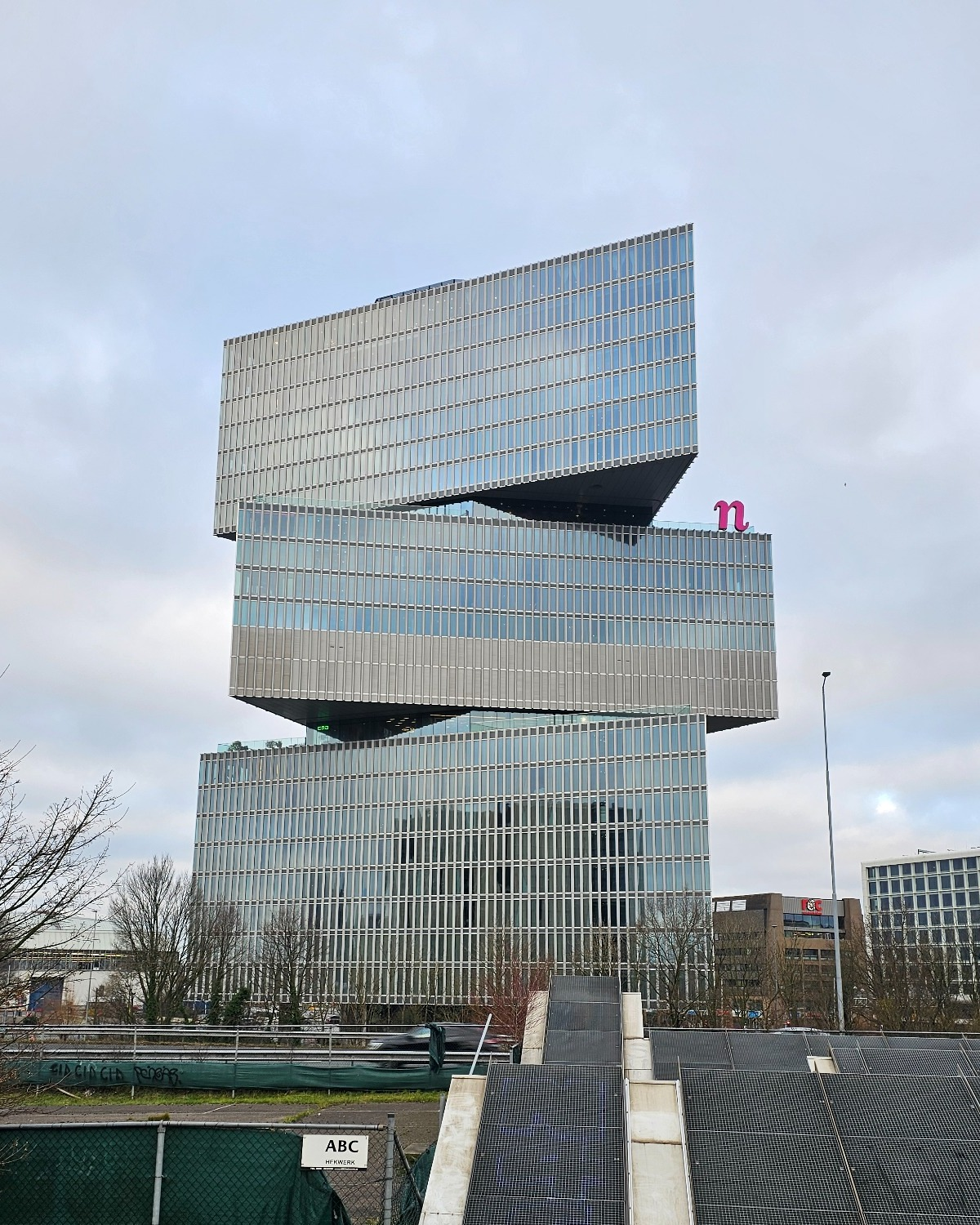Three glass-clad building sections are stacked at angles above a canal-side construction site.