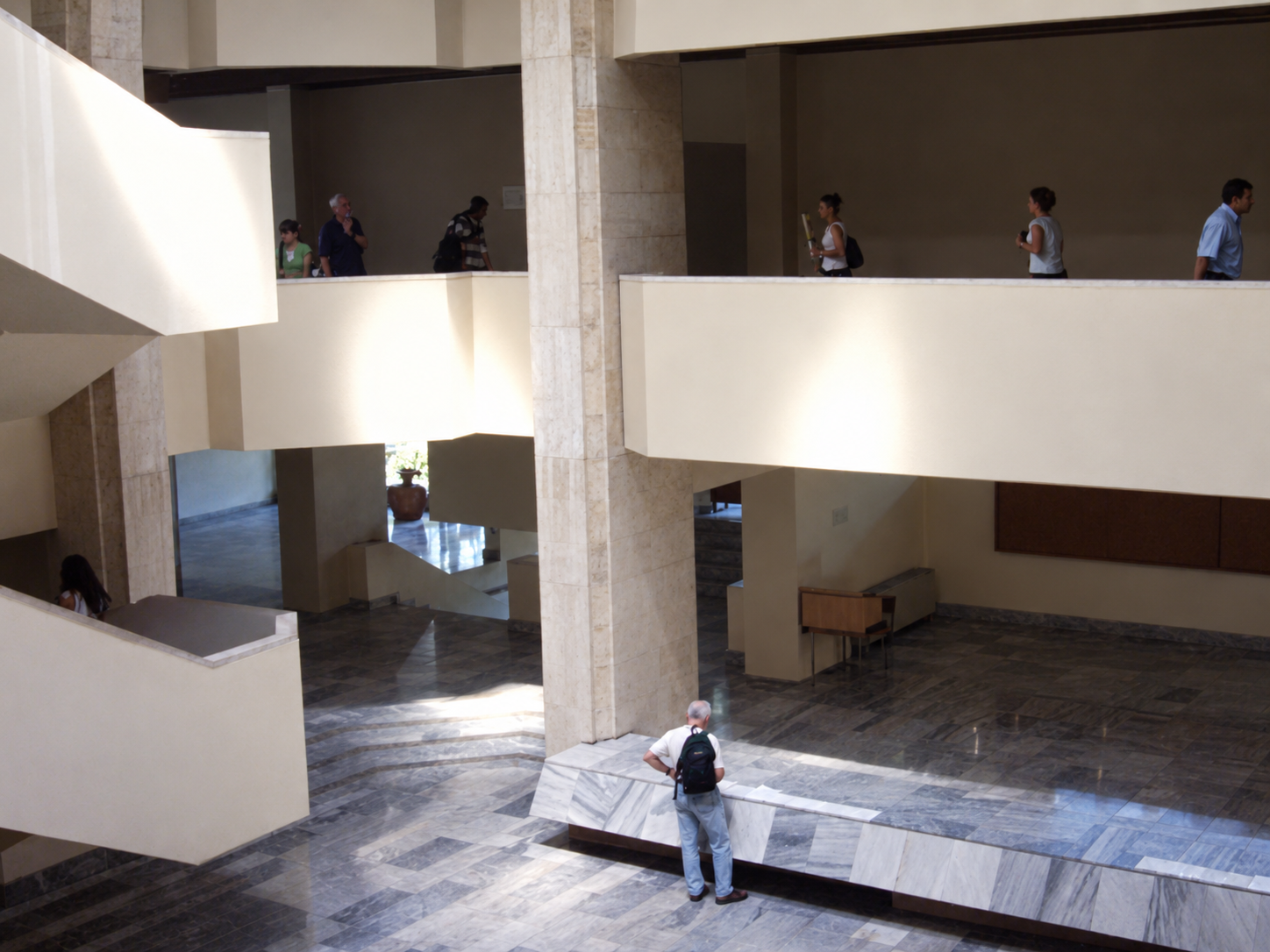 People stand on balconies in a marble atrium, with one person below, in a faculty building in Plovdiv.