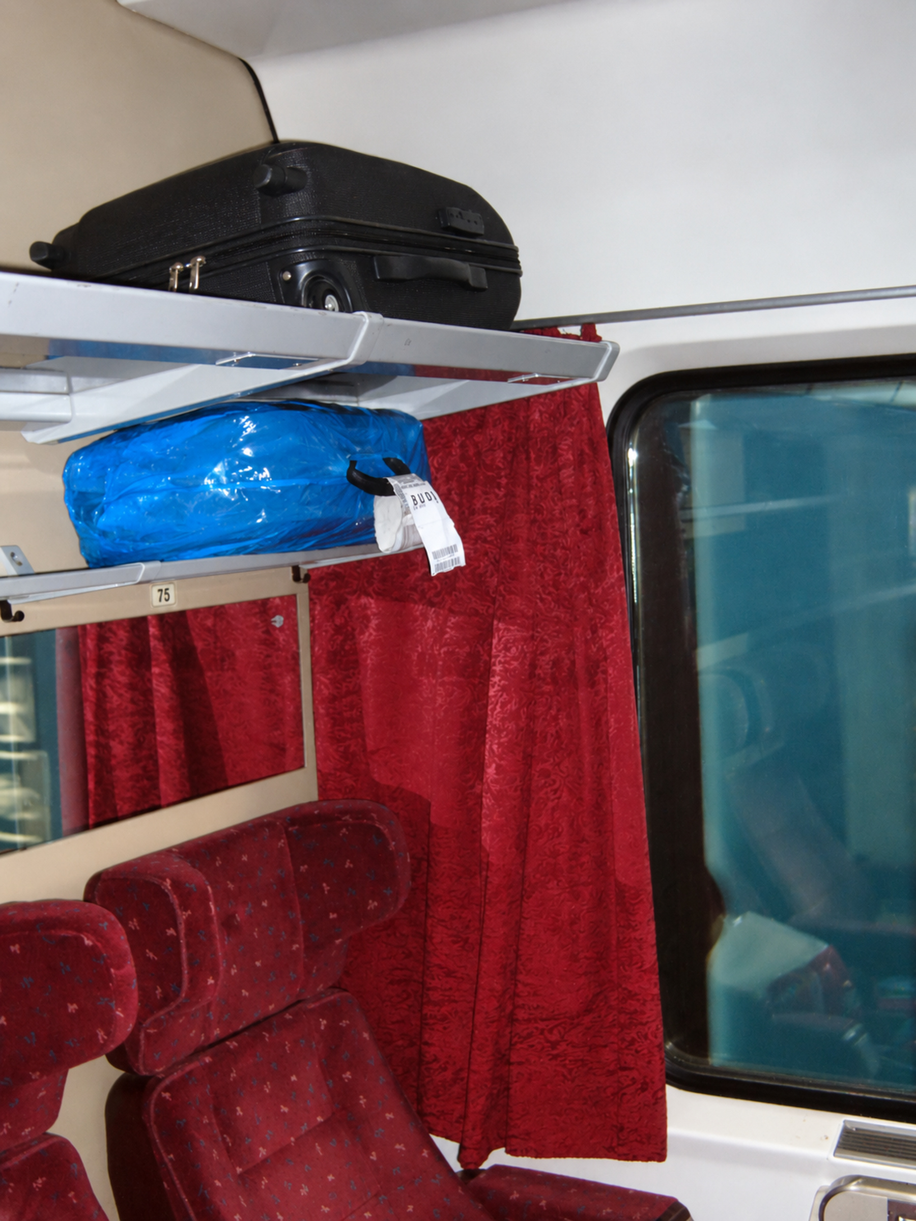 Luggage on an overhead rack beside red train seats and a window