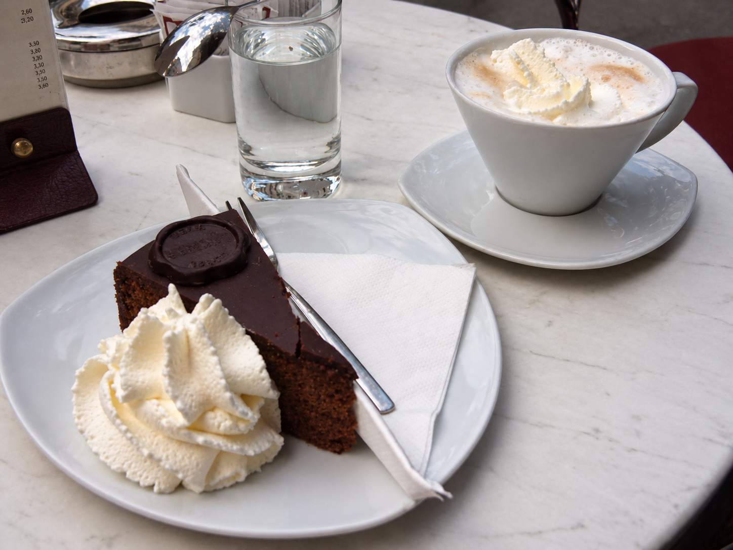 Sachertorte with whipped cream, coffee, and water on a café table in Vienna.