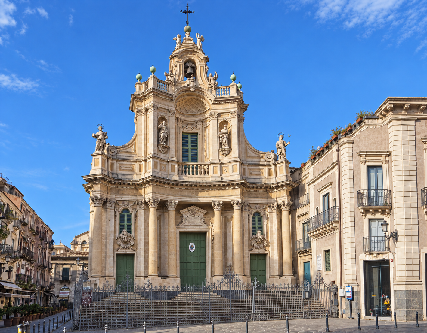 Basilica della Collegiata in Catania, with its ornate Baroque façade and statues facing a fenced square.