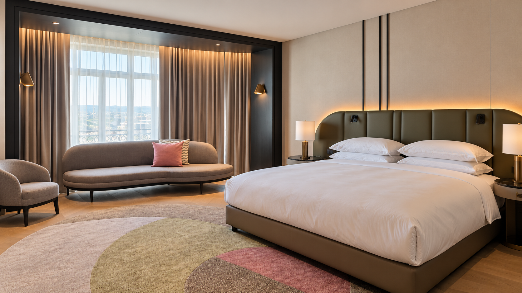Hotel room with a large bed, curved sofa, armchairs, and railway station visible through the window in Luxembourg
