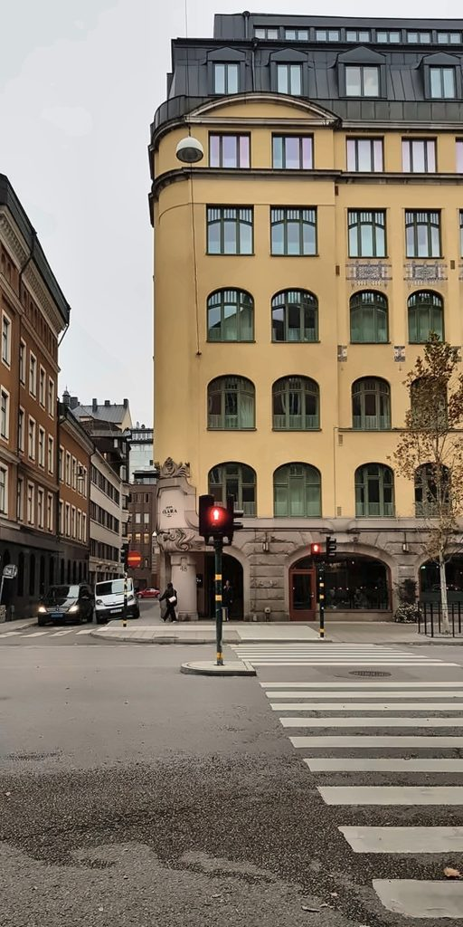Yellow rounded-corner building beside a crosswalk and traffic light on a Stockholm street.