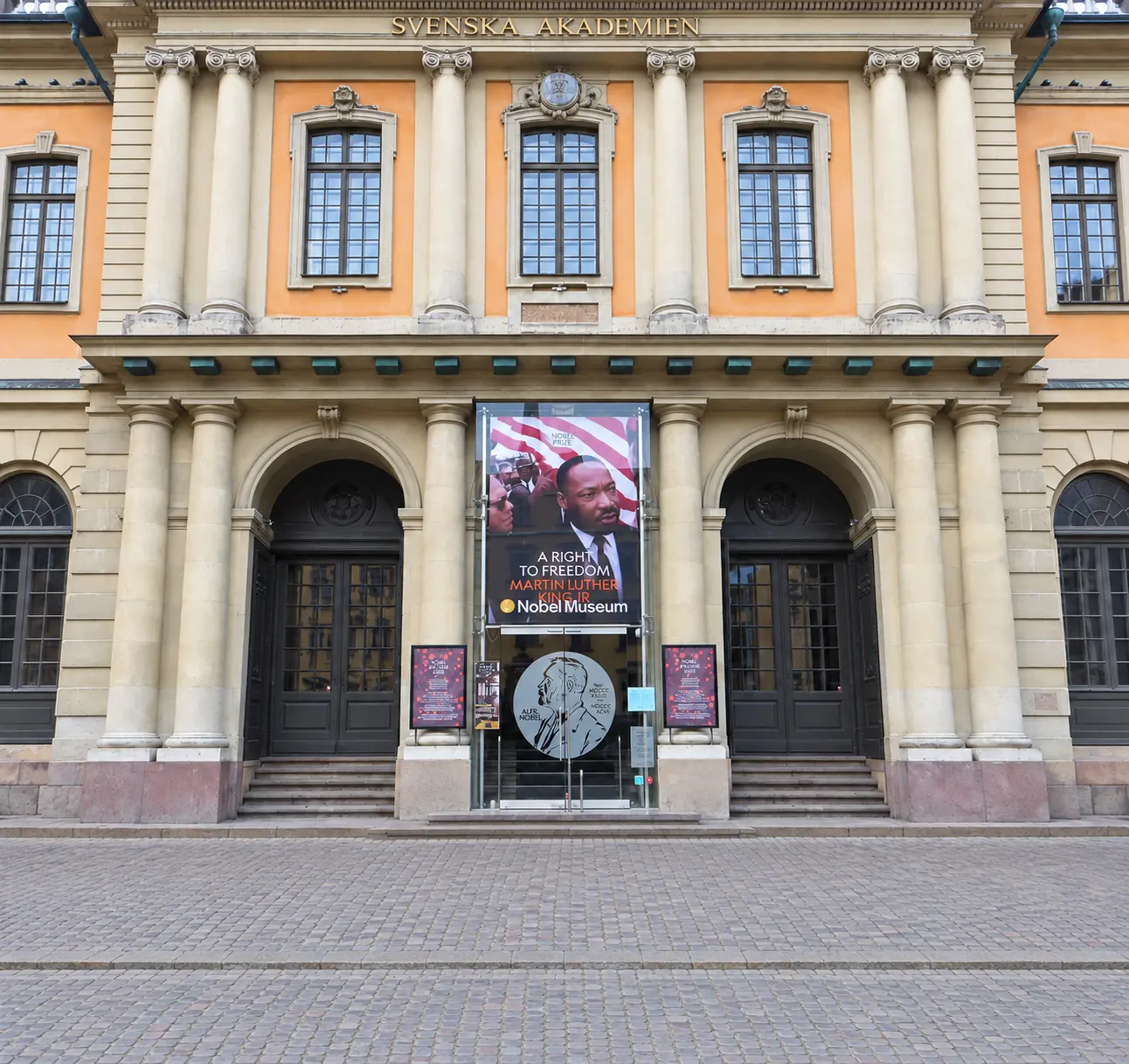 Swedish Academy facade in Stockholm, with columns, tall windows, and Nobel Prize Museum banners at the entrance.