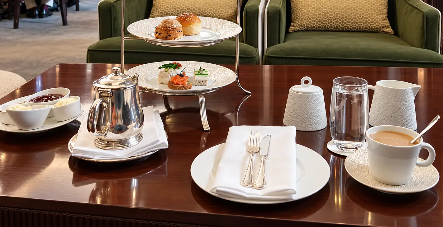 Afternoon tea with pastries, a silver teapot and teacup on a polished table at Stockholm’s Grand Hôtel.