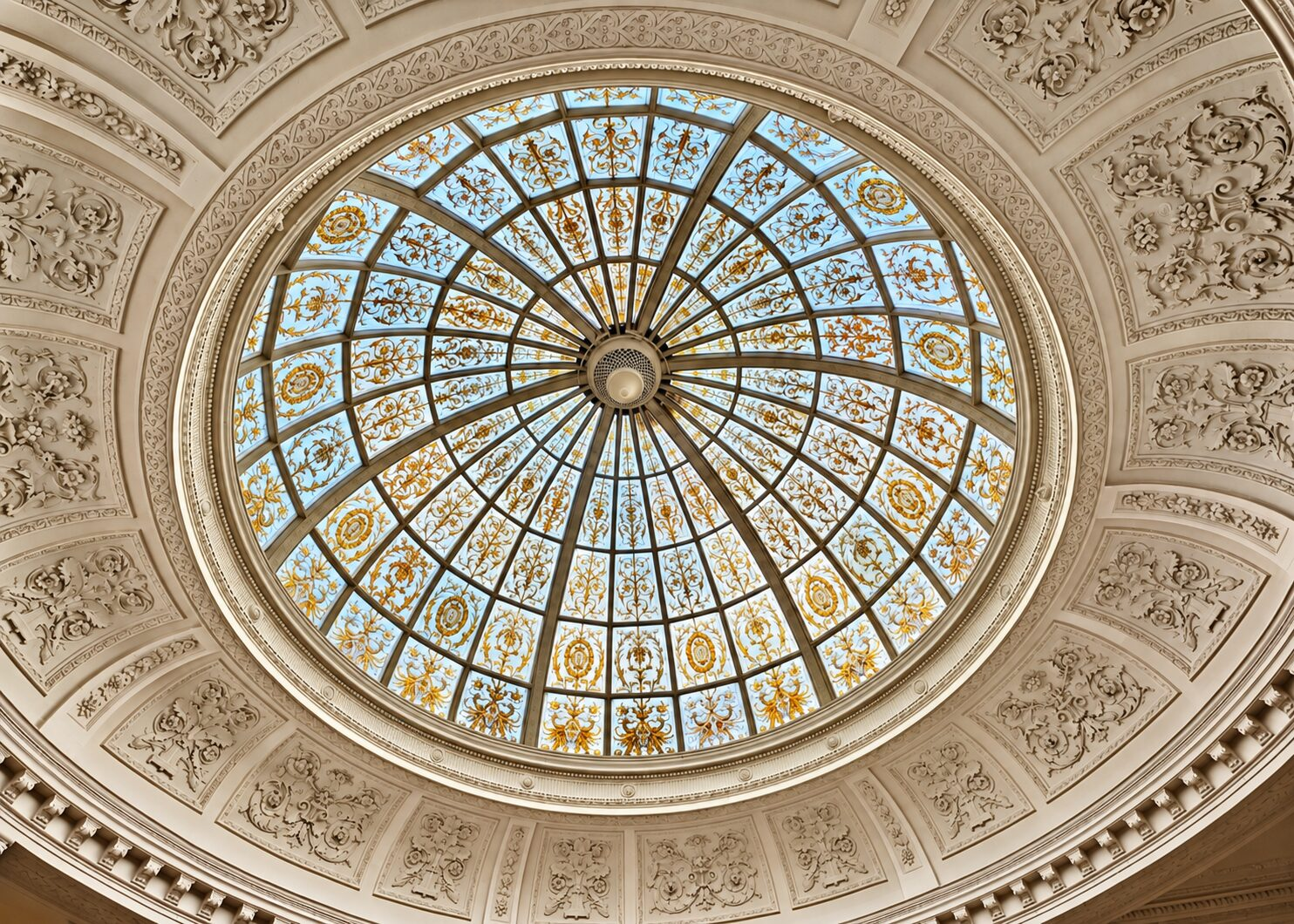Stained-glass dome with blue and gold panels, surrounded by ornate white ceiling decoration at Threadneedles.