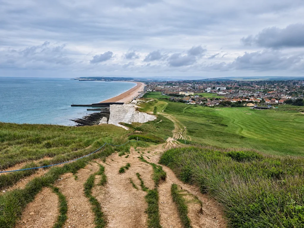 Coastal footpath overlooking Seaford, East Sussex, with the beach, sea, breakwaters and town below.