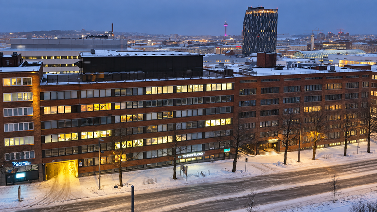 Snow-covered Tampere street and brick office buildings at dusk, with a tall tower and city lights in the background.