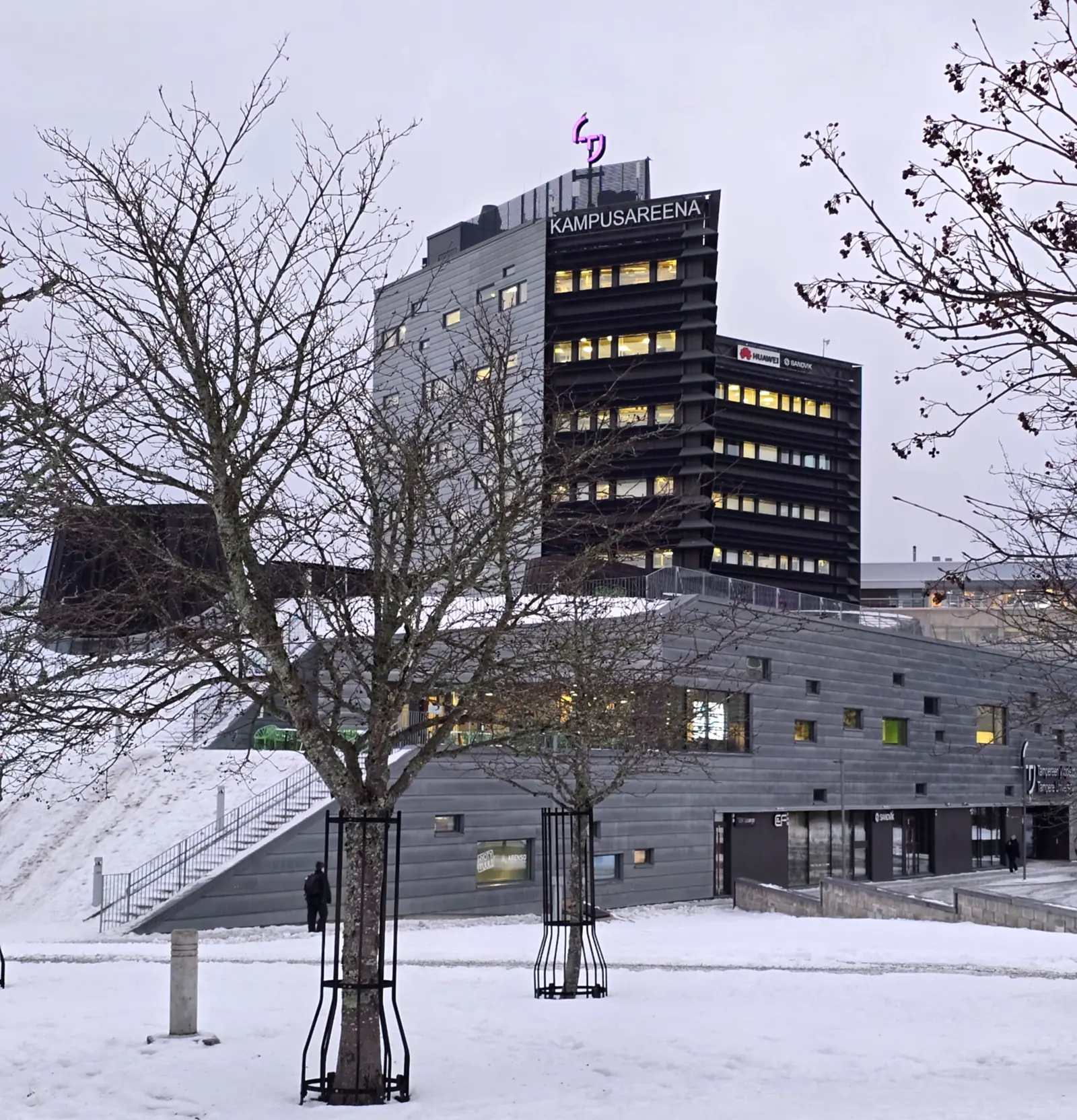 Kampusareena building at Tampere University, seen behind snow-covered grounds and leafless trees.
