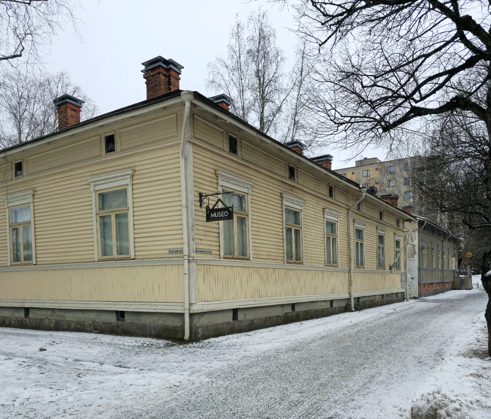 Wooden workers’ block in snowy Amuri, Tampere, with a modern apartment building behind it.