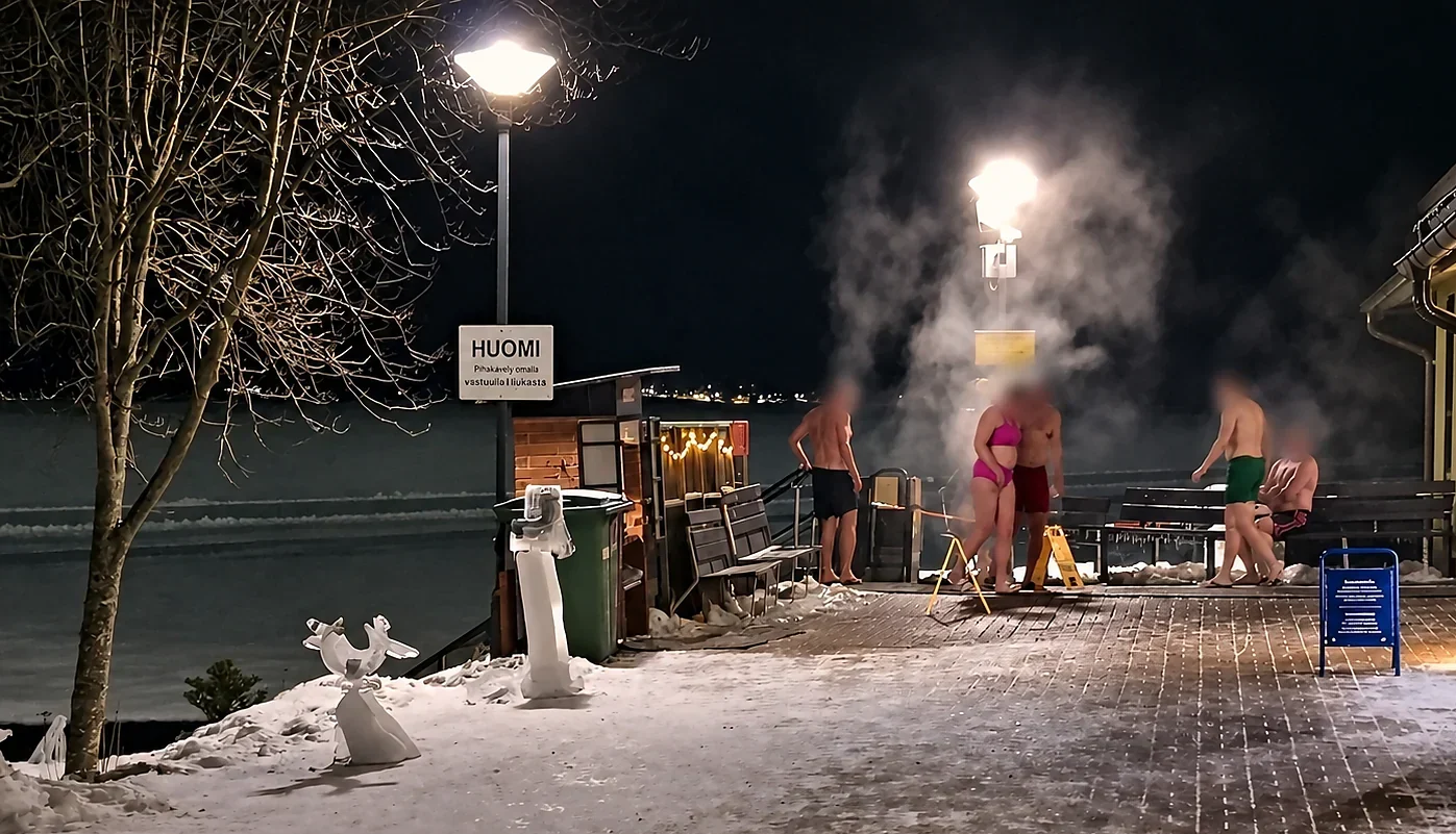 People in swimwear stand by a steaming sauna and snowy lakeside swimming hole at Kaupinoja, Tampere.