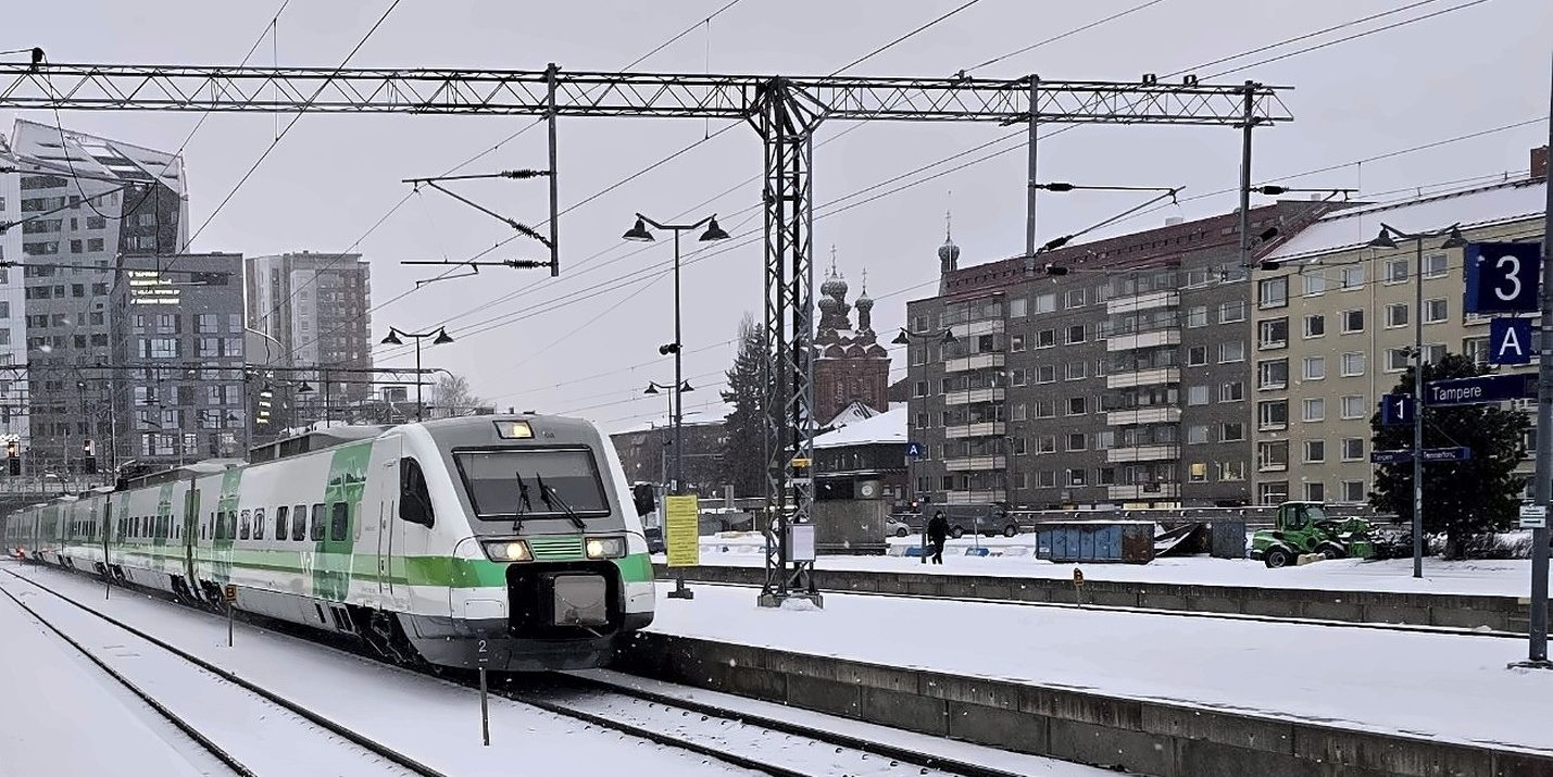 Green-and-white commuter train arrives at a snow-covered station in Tampere, Finland.
