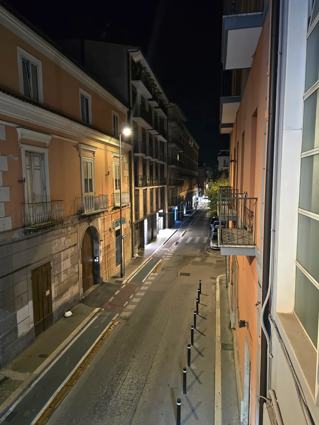 Night view of a quiet street lined with historic buildings, balconies, and streetlights in Caserta.