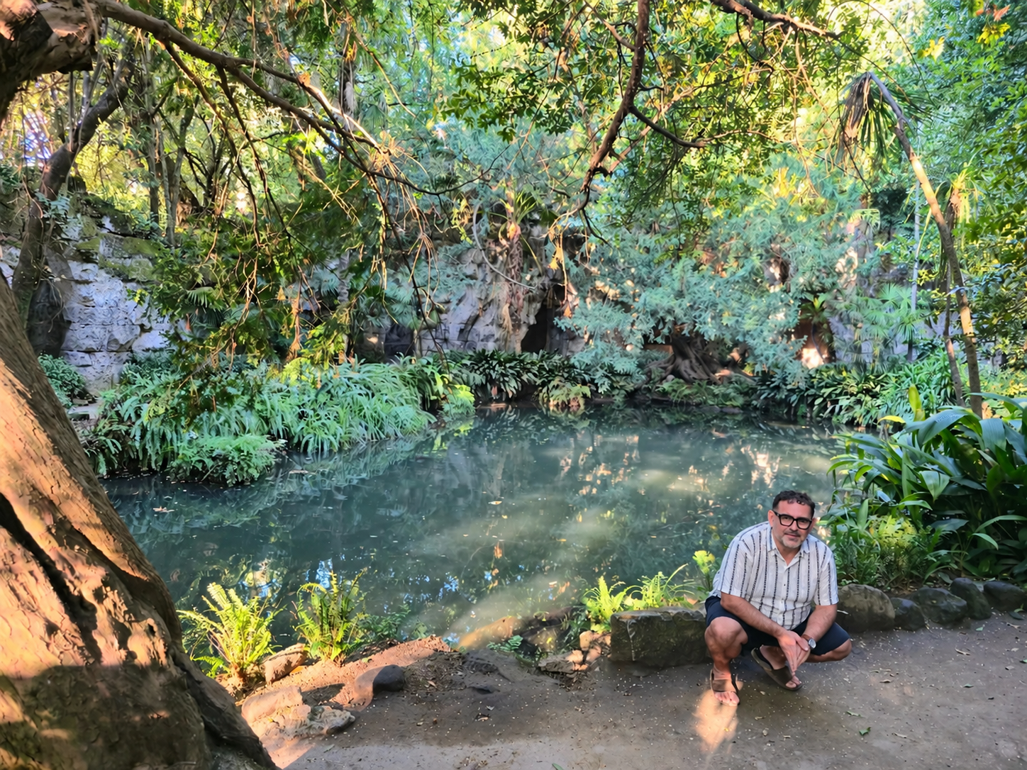 Man in a striped shirt crouches beside the pond at Bagno di Venere in Caserta.