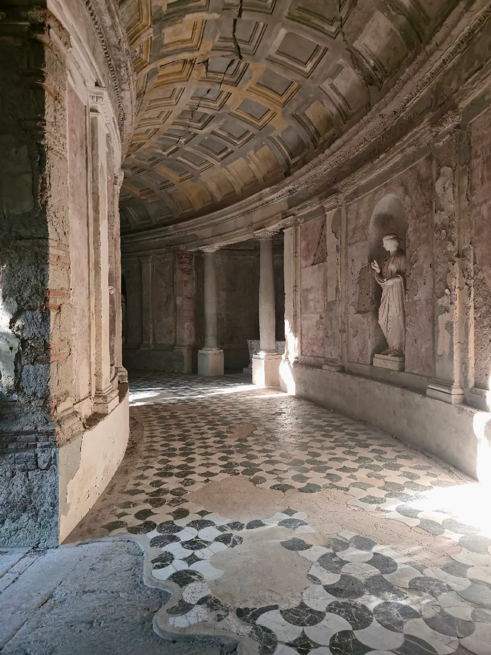 Mosaic-floored cryptoporticus with columns, wall niches, statues, and a coffered barrel vault.