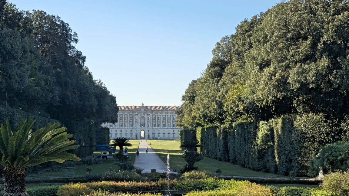The Reggia di Caserta stands beyond a formal garden path lined with hedges and trees.