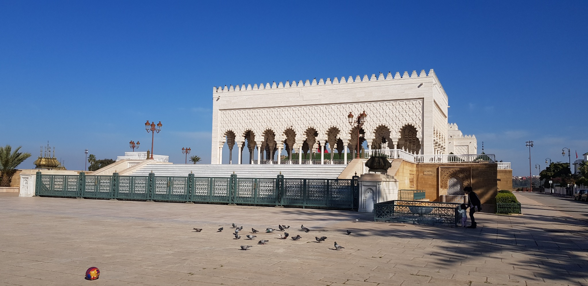 White crenellated building with arched columns beside a tiled railing in Rabat; pigeons dot the plaza.