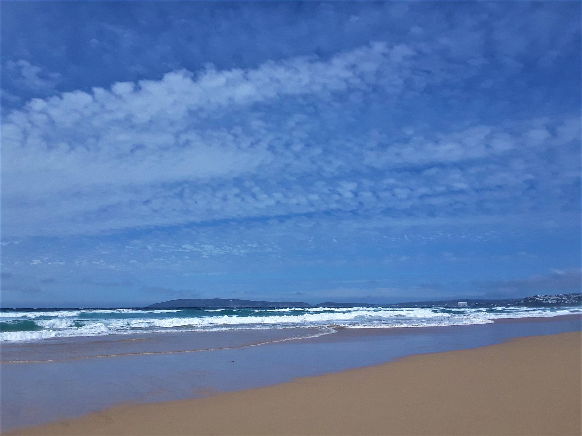 Vast open expanse of sandy white beach on the south coast of Africa with the town of Plettenberg Bay on the right