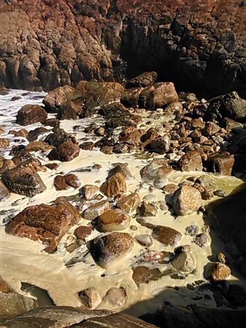 Fascinating foam build-up as the ocean churns in the swell among the rocks at the shoreline.